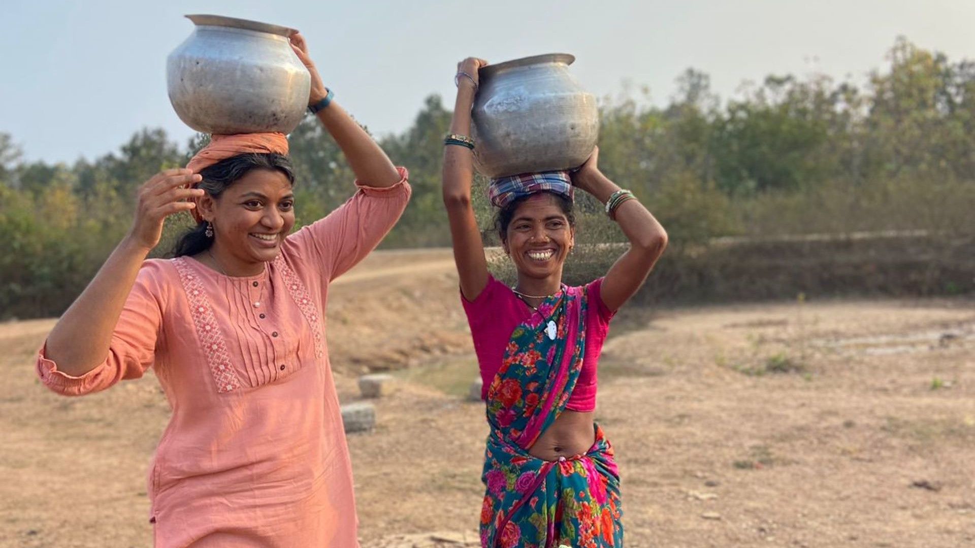 Two women balance large pots on their heads